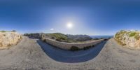 360 view lens image of a stone road, next to a rock mountain range with the sun shining on the horizon