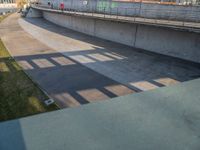 a skateboarder riding on a cement ramp next to a city street under a bridge