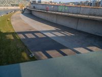 a skateboarder riding on a cement ramp next to a city street under a bridge