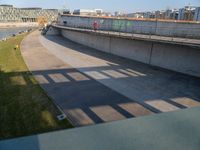 a skateboarder riding on a cement ramp next to a city street under a bridge