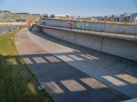 a skateboarder riding on a cement ramp next to a city street under a bridge