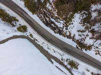 a truck is driving on the road through a snow covered mountain and evergreen forest below