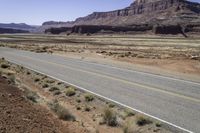 a person riding a motorcycle down a desert road near cliffs and sand dunes a black bear is standing in the distance