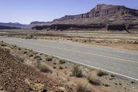 a person riding a motorcycle down a desert road near cliffs and sand dunes a black bear is standing in the distance