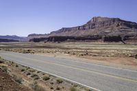 a person riding a motorcycle down a desert road near cliffs and sand dunes a black bear is standing in the distance