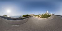 fish eye view of street in front of lighthouse and cliff side in the background is the sun