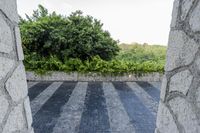 a black and white striped floor near a stone wall and plants with trees in the background