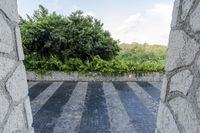 a black and white striped floor near a stone wall and plants with trees in the background