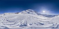 a mountain with snow and blue sky with snow covered peaks in the background and moon in the background