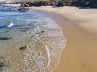 a beach with several small waves and white sand in front of it and some blue sky