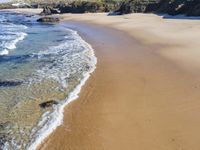 a beach with several small waves and white sand in front of it and some blue sky