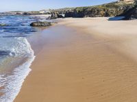 a beach with several small waves and white sand in front of it and some blue sky