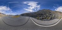 a 360 - view image of an asphalt road through some rocks and bushes with clouds