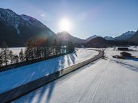 there is snow on the ground in front of the mountains and village with sun shining over the city