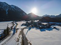 there is snow on the ground in front of the mountains and village with sun shining over the city