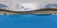 a tennis court is covered in blue water with a sky background and clouds above it