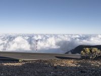 a man standing on top of a hill next to a highway below clouds in the distance