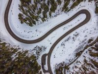 an aerial view of a winding road near a forested forest area and a snow covered mountain top