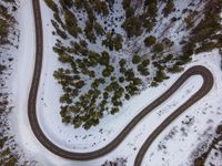 an aerial view of a winding road near a forested forest area and a snow covered mountain top