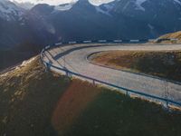 a mountain view shows a long winding road with traffic going through it, alongside a forested mountain range