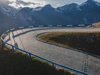 a mountain view shows a long winding road with traffic going through it, alongside a forested mountain range