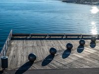 five metal spheres sit on the deck by the water, with a few buildings in the background