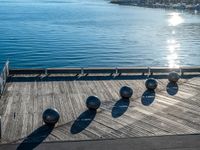 five metal spheres sit on the deck by the water, with a few buildings in the background