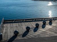 five metal spheres sit on the deck by the water, with a few buildings in the background