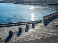 five metal spheres sit on the deck by the water, with a few buildings in the background