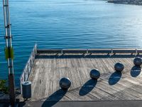 five metal spheres sit on the deck by the water, with a few buildings in the background