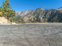 an empty asphalt parking lot with mountains in the background of it, and a blue sky overhead