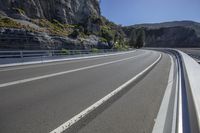 the empty highway is running alongside the rock cliff wall as a cyclist rides down it