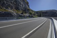 the empty highway is running alongside the rock cliff wall as a cyclist rides down it