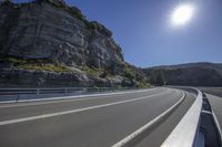 the empty highway is running alongside the rock cliff wall as a cyclist rides down it