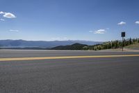 an empty asphalt road and mountain view in the distance, with a sign on it