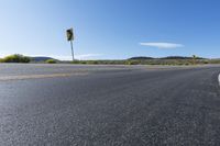 an empty asphalt road with yellow stripes on one side and hills in the other side