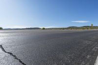 an empty asphalt road with yellow stripes on one side and hills in the other side