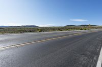 an empty asphalt road with yellow stripes on one side and hills in the other side