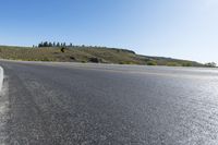 an empty asphalt road with yellow stripes on one side and hills in the other side