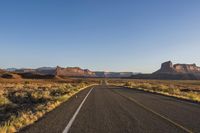 there is an empty asphalt road next to some desert rocks and grass in the distance there is a sky