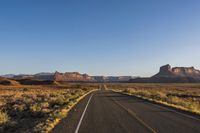 there is an empty asphalt road next to some desert rocks and grass in the distance there is a sky