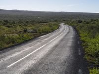 an empty, asphalt road runs through an arid landscape on a sunny day in iceland