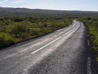 an empty, asphalt road runs through an arid landscape on a sunny day in iceland