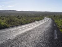 an empty, asphalt road runs through an arid landscape on a sunny day in iceland