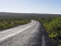 an empty, asphalt road runs through an arid landscape on a sunny day in iceland