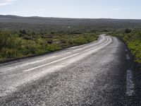 an empty, asphalt road runs through an arid landscape on a sunny day in iceland