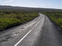 an empty, asphalt road runs through an arid landscape on a sunny day in iceland