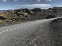 an empty asphalt road with rocks in the distance under blue cloudy skies near lava and green mountains