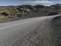 an empty asphalt road with rocks in the distance under blue cloudy skies near lava and green mountains