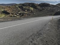 an empty asphalt road with rocks in the distance under blue cloudy skies near lava and green mountains